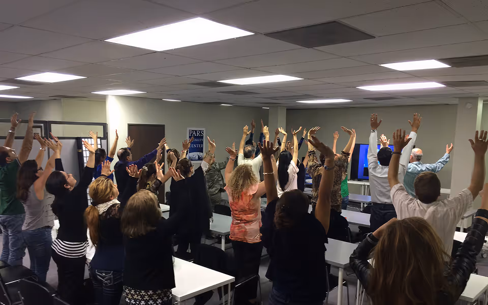 Group of people in a classroom raising their hands above their heads, participating actively.