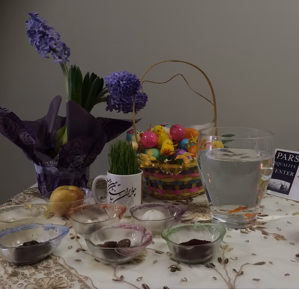 Traditional Haft-Seen table with purple flowers, green sprouts, apple, bowls, basket, and a glass of water with fish.