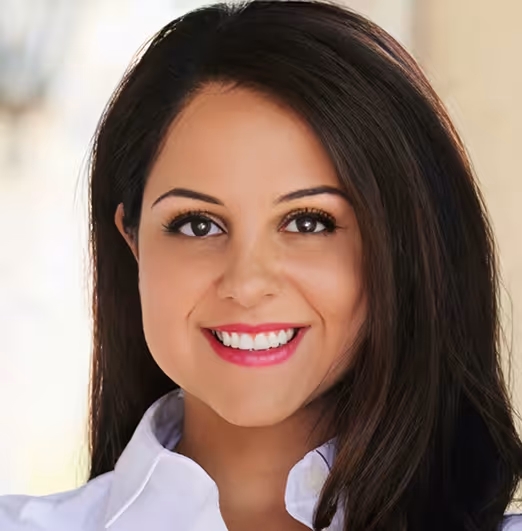 Smiling woman with long dark hair and white shirt against a light blurred background.