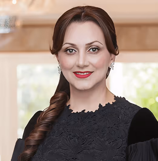Smiling woman with long curled hair wearing black lace dress and red lipstick indoors.