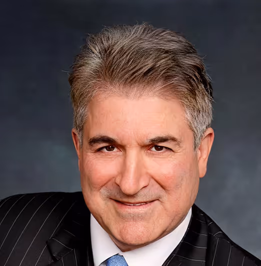 Portrait of middle-aged man with gray hair wearing a striped suit and blue tie against dark background.