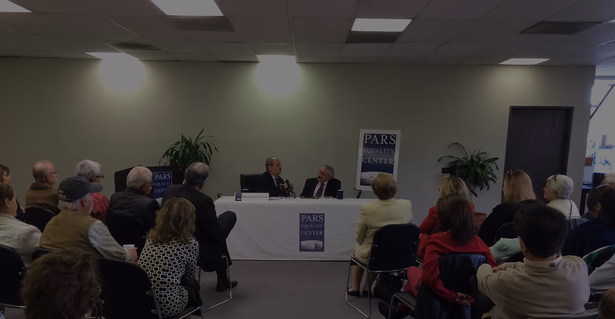 Audience attending a panel discussion at Pars Equality Center with two speakers at a table.