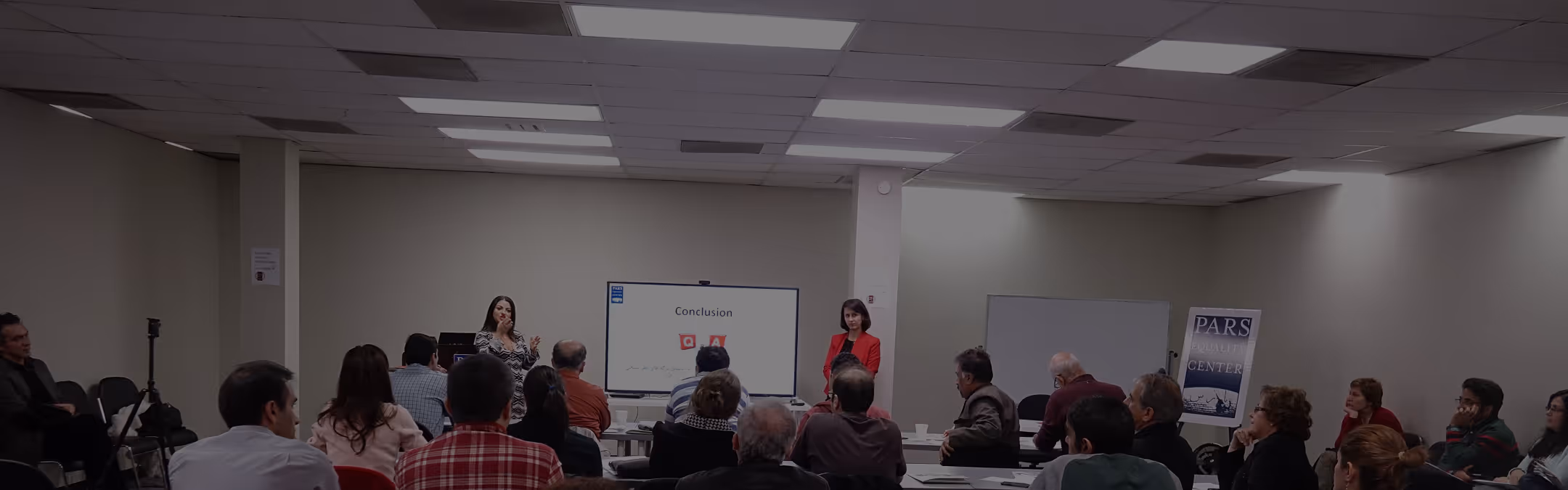Audience attending a presentation with two female speakers in a conference room.