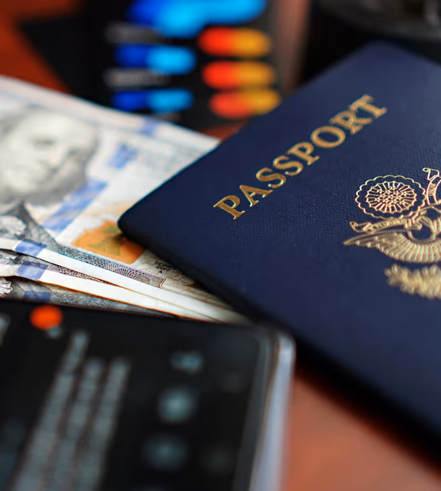 Close-up of a passport, US dollar bills, and a blurred smartphone on a table.