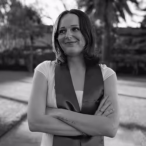 Young woman with crossed arms smiling outdoors, wearing a stole around her neck.