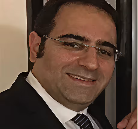 Smiling man with glasses in a suit and striped tie in an indoor setting.