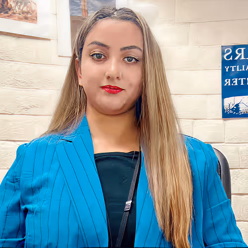 Woman with long blonde hair wearing a blue pinstripe blazer and red lipstick indoors.