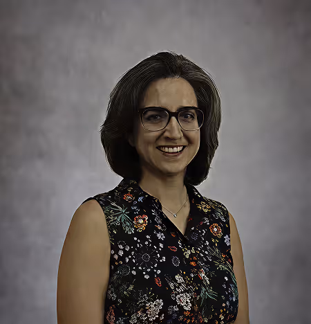 Smiling woman with glasses wearing a black floral sleeveless top against a gray background.