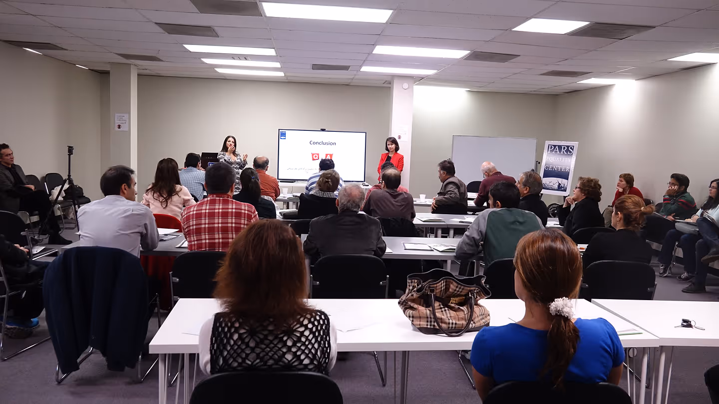 People sit at tables facing two presenters in a conference room with a screen showing a Q&A slide.