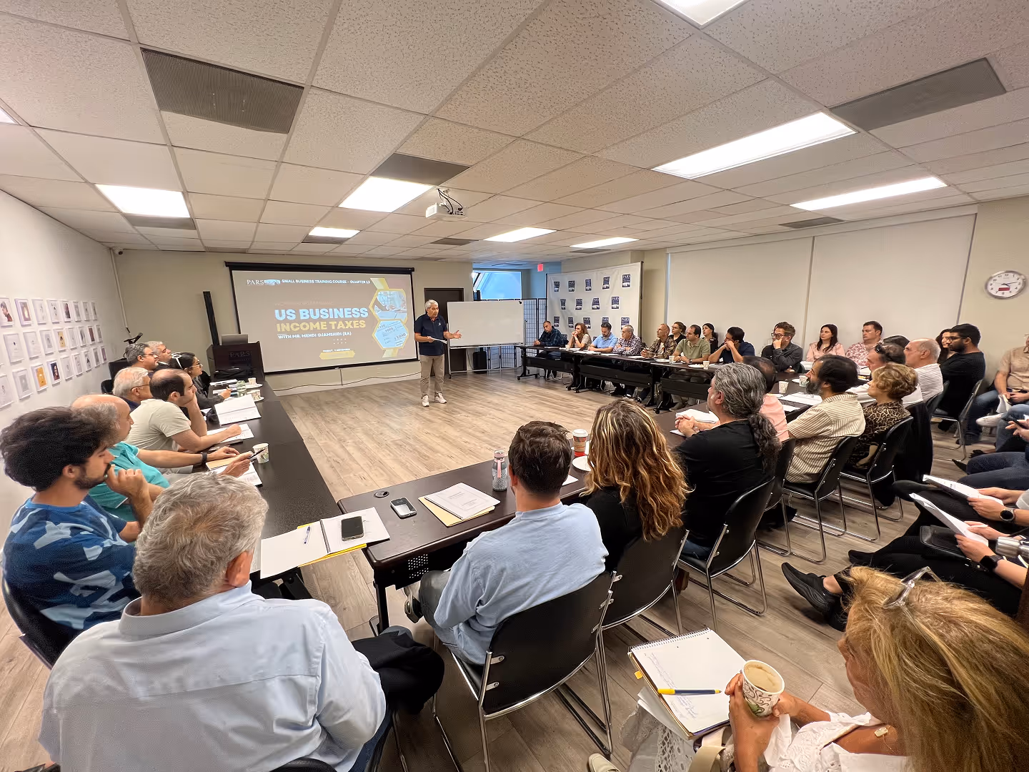 Instructor teaching a US Business Income Taxes course to a diverse adult class seated in a conference room.