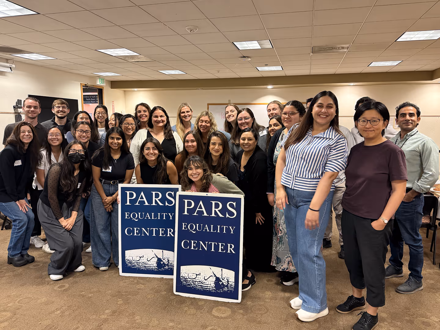 Group of diverse people posing indoors with two blue signs reading PARS Equality Center.