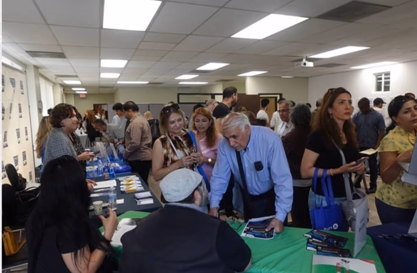 People interacting and networking at a busy indoor event with tables and informational materials.