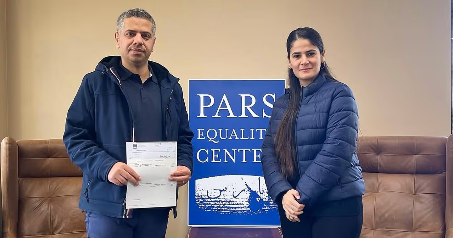 Man holding document and woman standing beside him with PARS Equality Center sign in background.