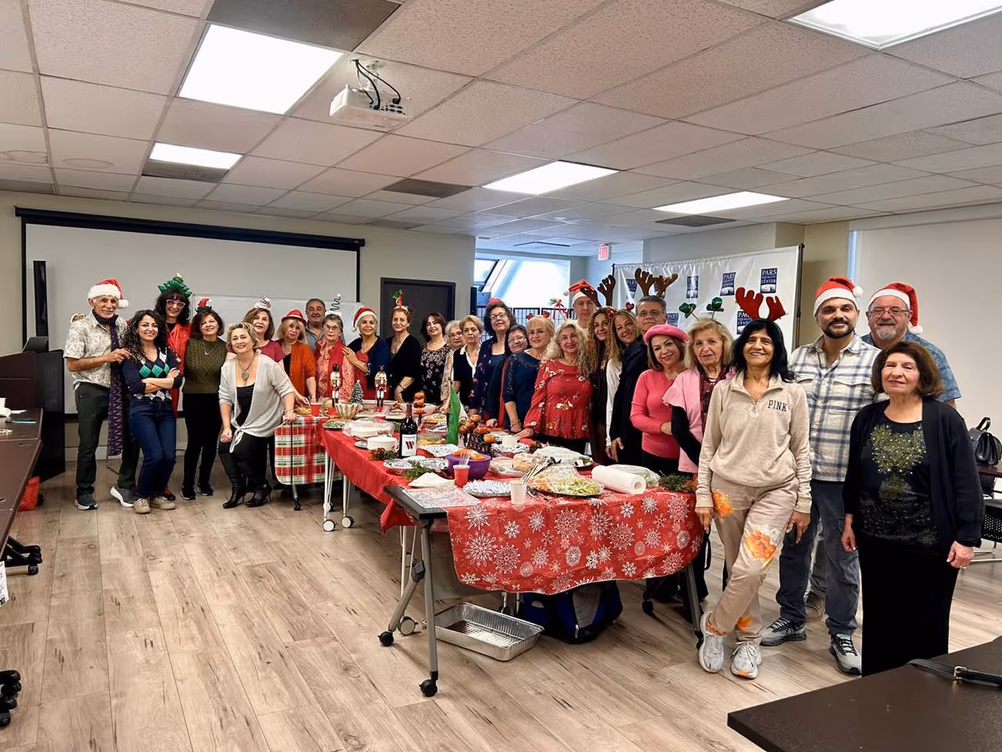 Group of adults wearing festive holiday hats posing around a table with Christmas-themed food.