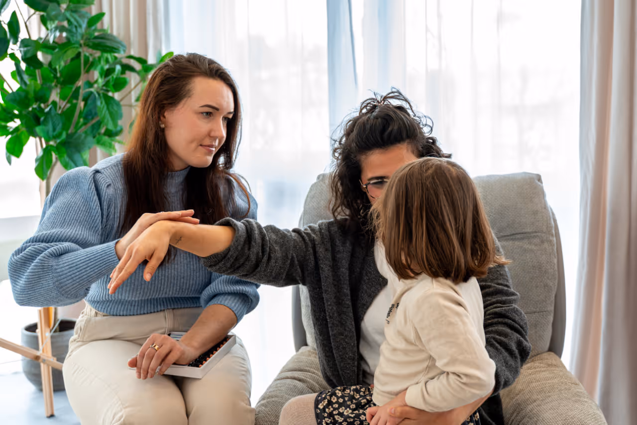 Eine Frau untersucht den Arm eines Kindes, während eine weitere Frau daneben sitzt und eine Abakus hält.