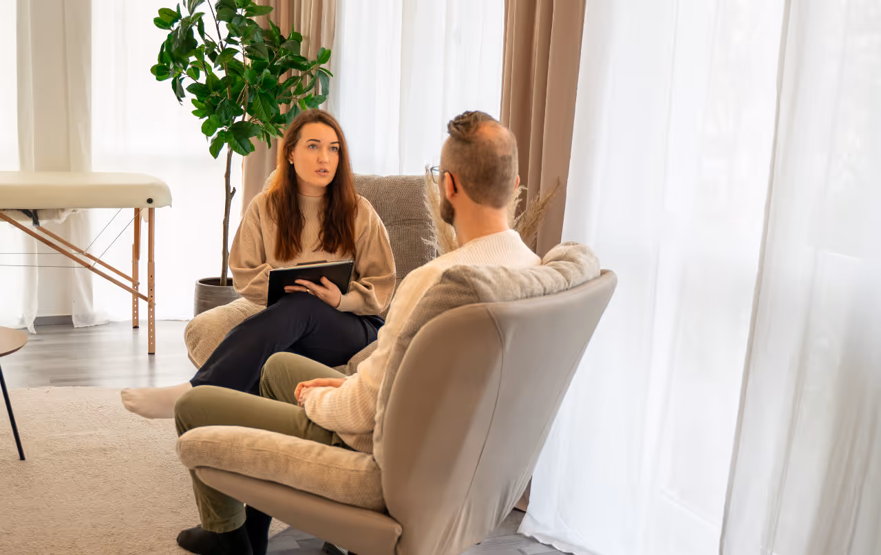 Eine Frau und ein Mann sitzen sich in einem gemütlichen Raum gegenüber und führen ein Gespräch.