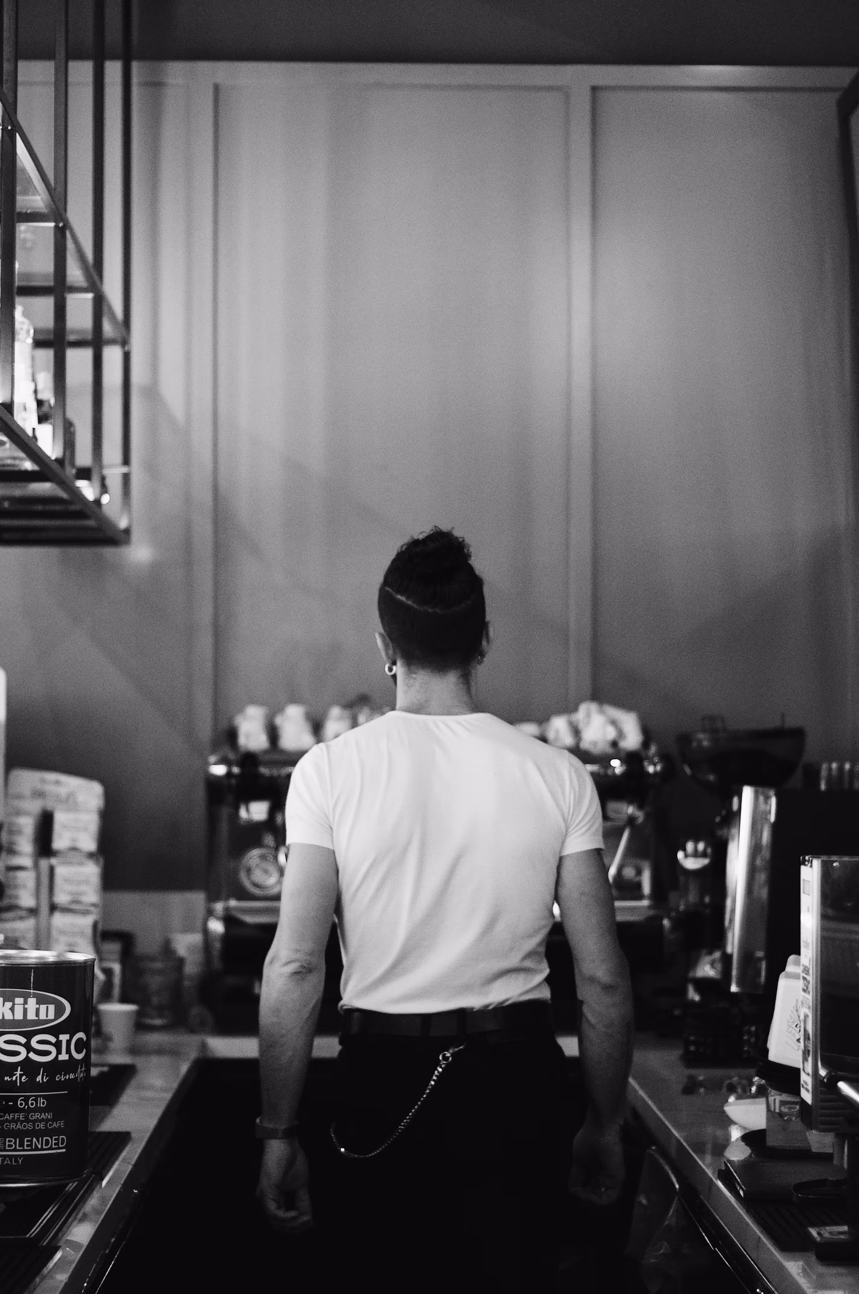 Man with a bun hairstyle standing behind a coffee counter with an espresso machine in front.