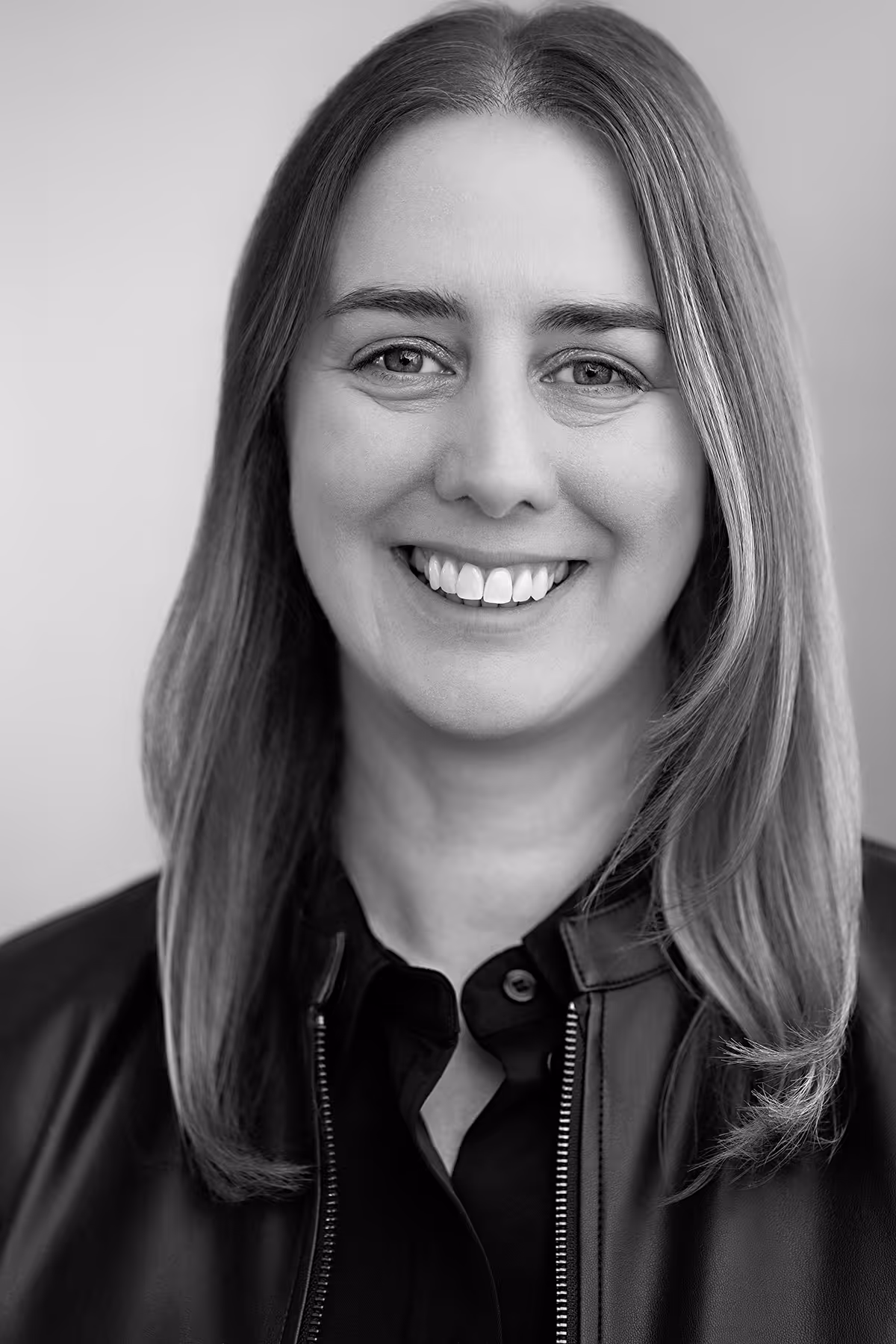 Smiling woman with straight shoulder-length hair wearing a black leather jacket and shirt.