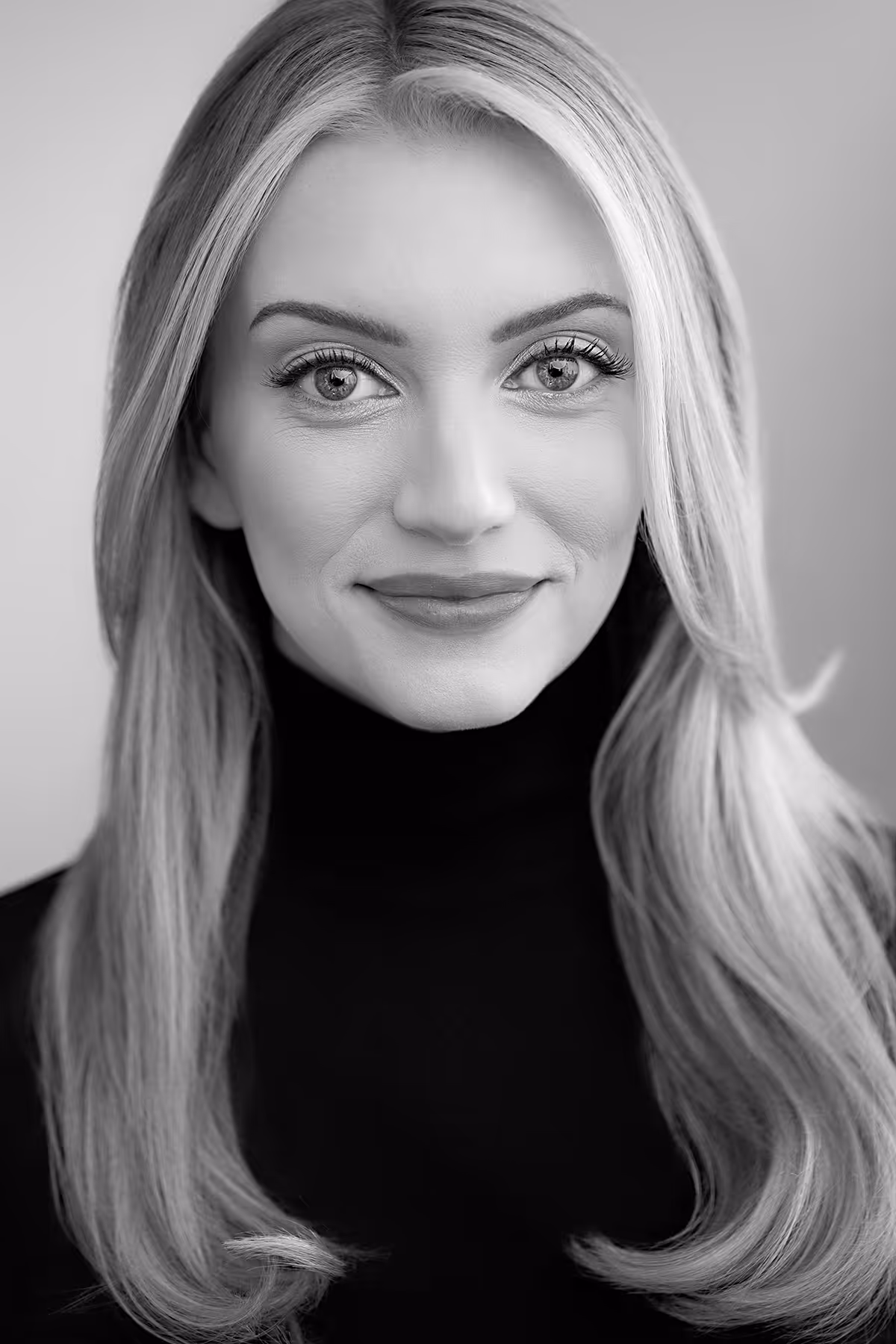 Black and white portrait of a smiling woman with long straight hair wearing a black turtleneck.