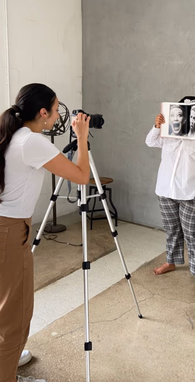 Person photographing another person who holds an open book in front of their face showing two black and white expressive faces.