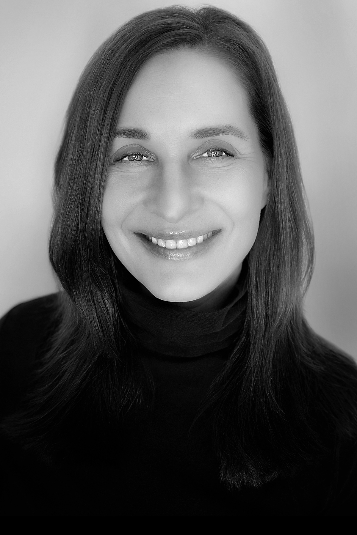 Black and white close-up portrait of a smiling woman with straight hair wearing a dark turtleneck.