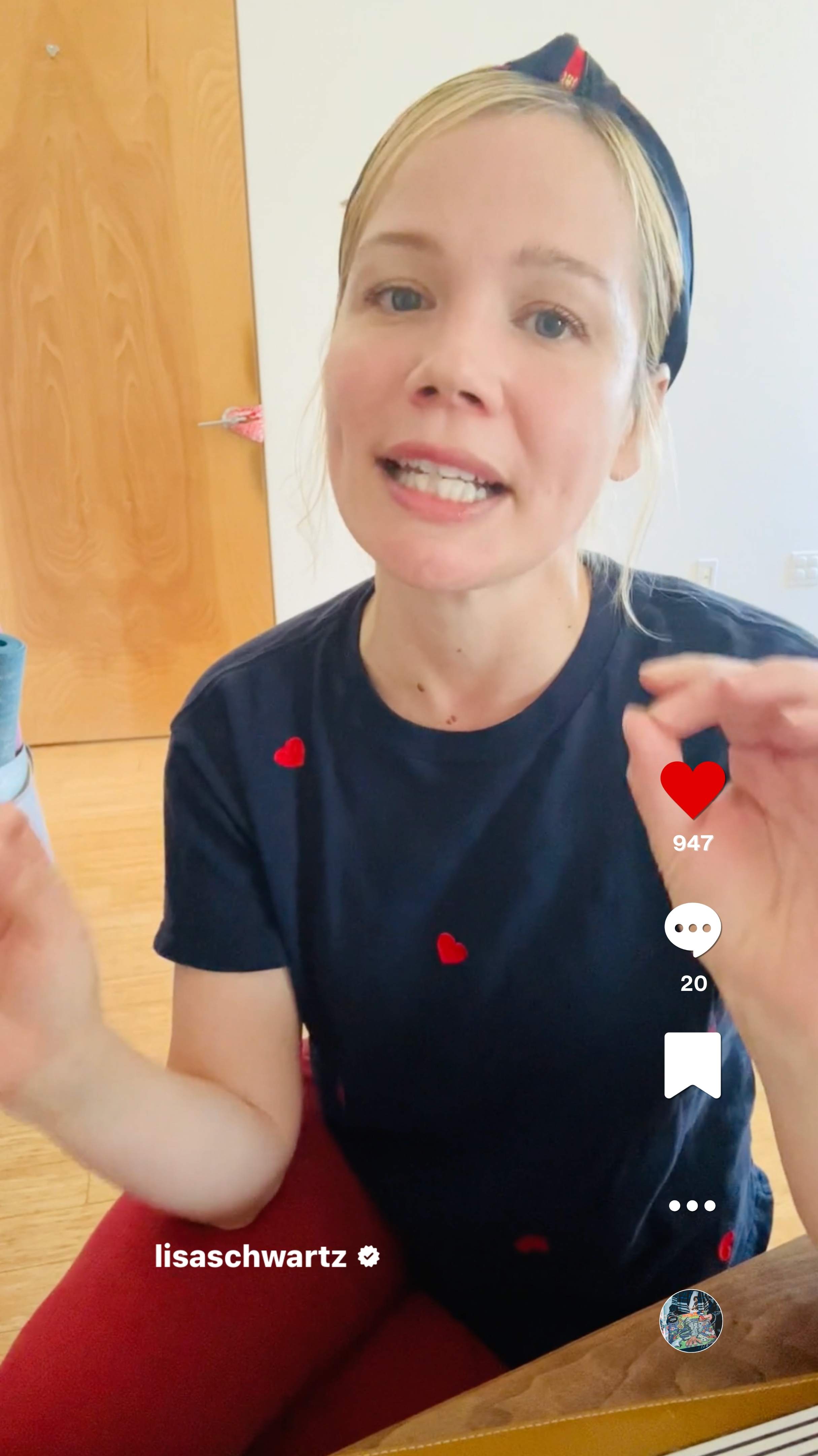 A woman with a headband and black shirt with red hearts gestures while speaking indoors.