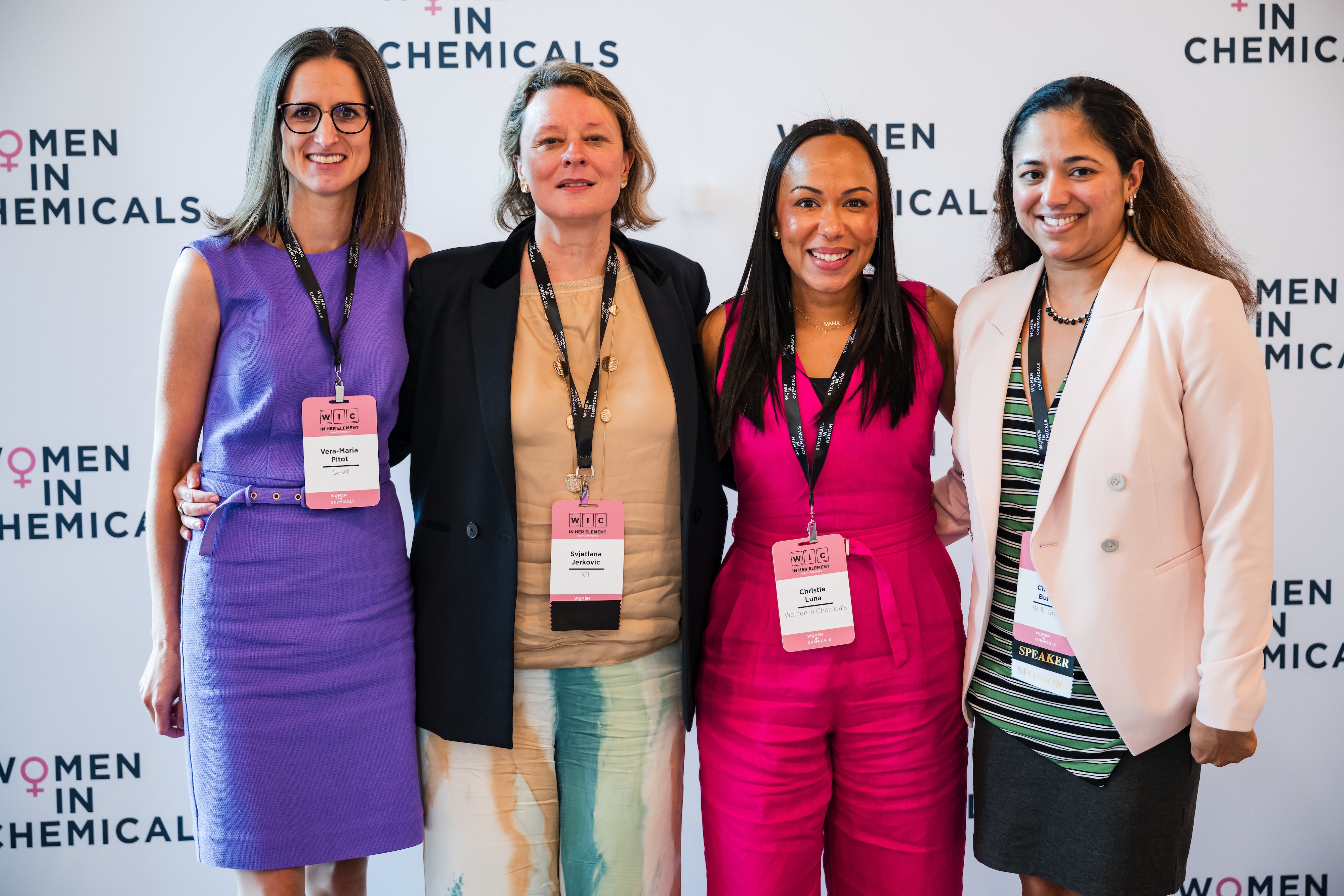 Four women pose for the camera in front of a wallpaper saying "Women In Chemicals."