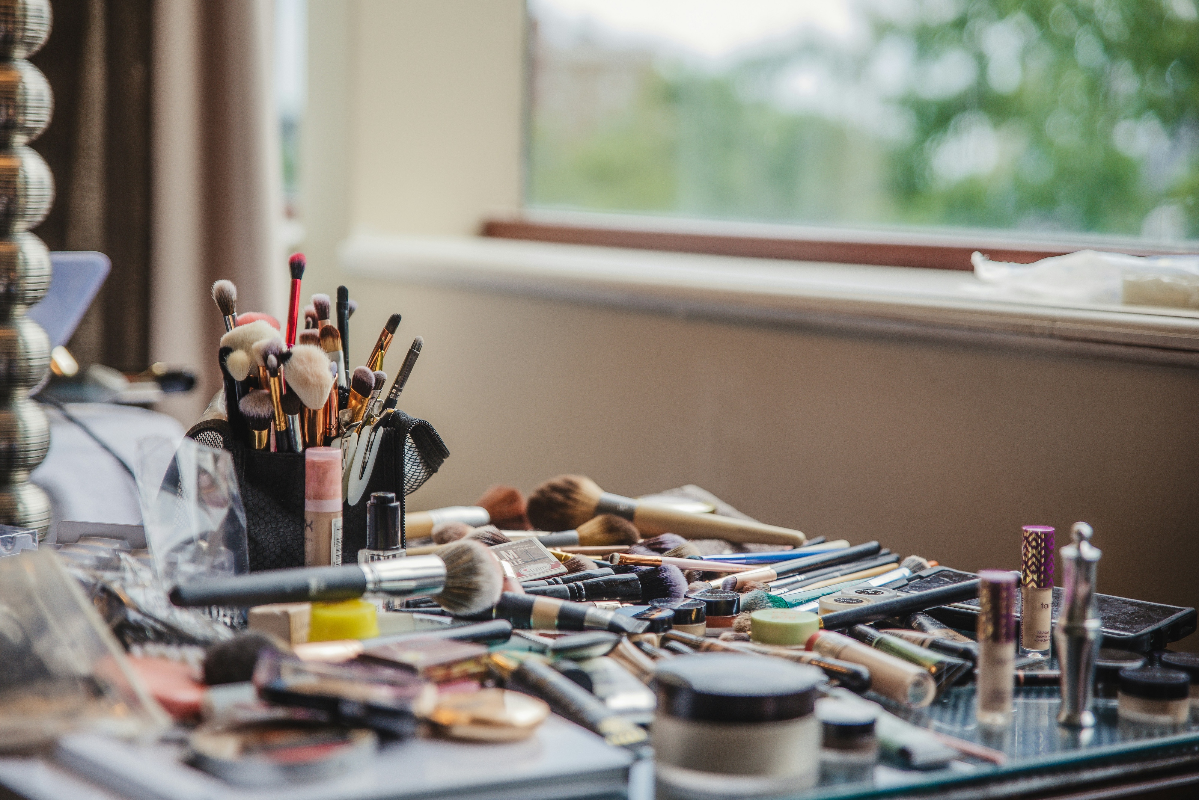 Makeup brushes lay scattered across a table by the window.