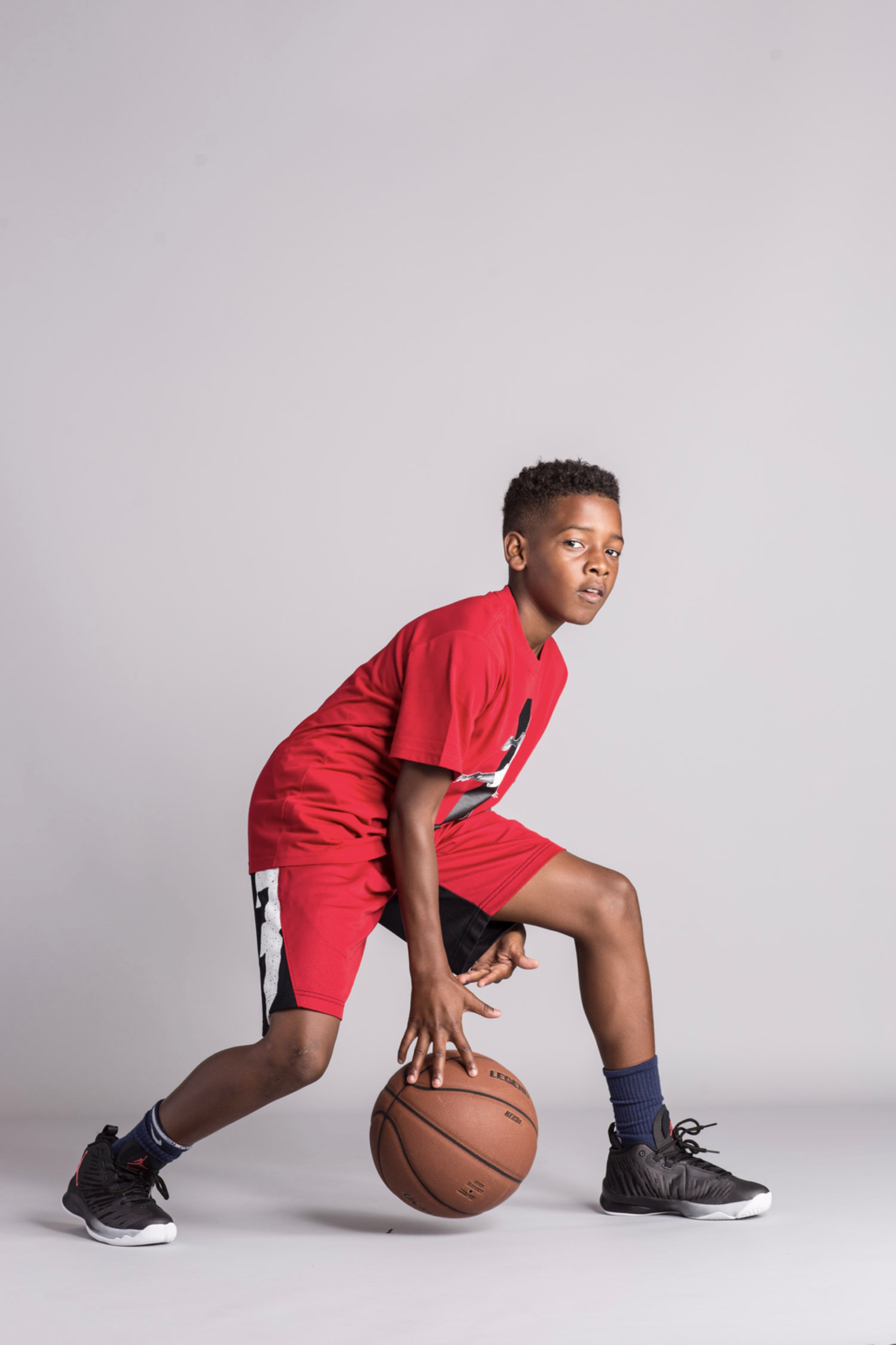 A boy wearing all red dribbles a basketball between his legs.