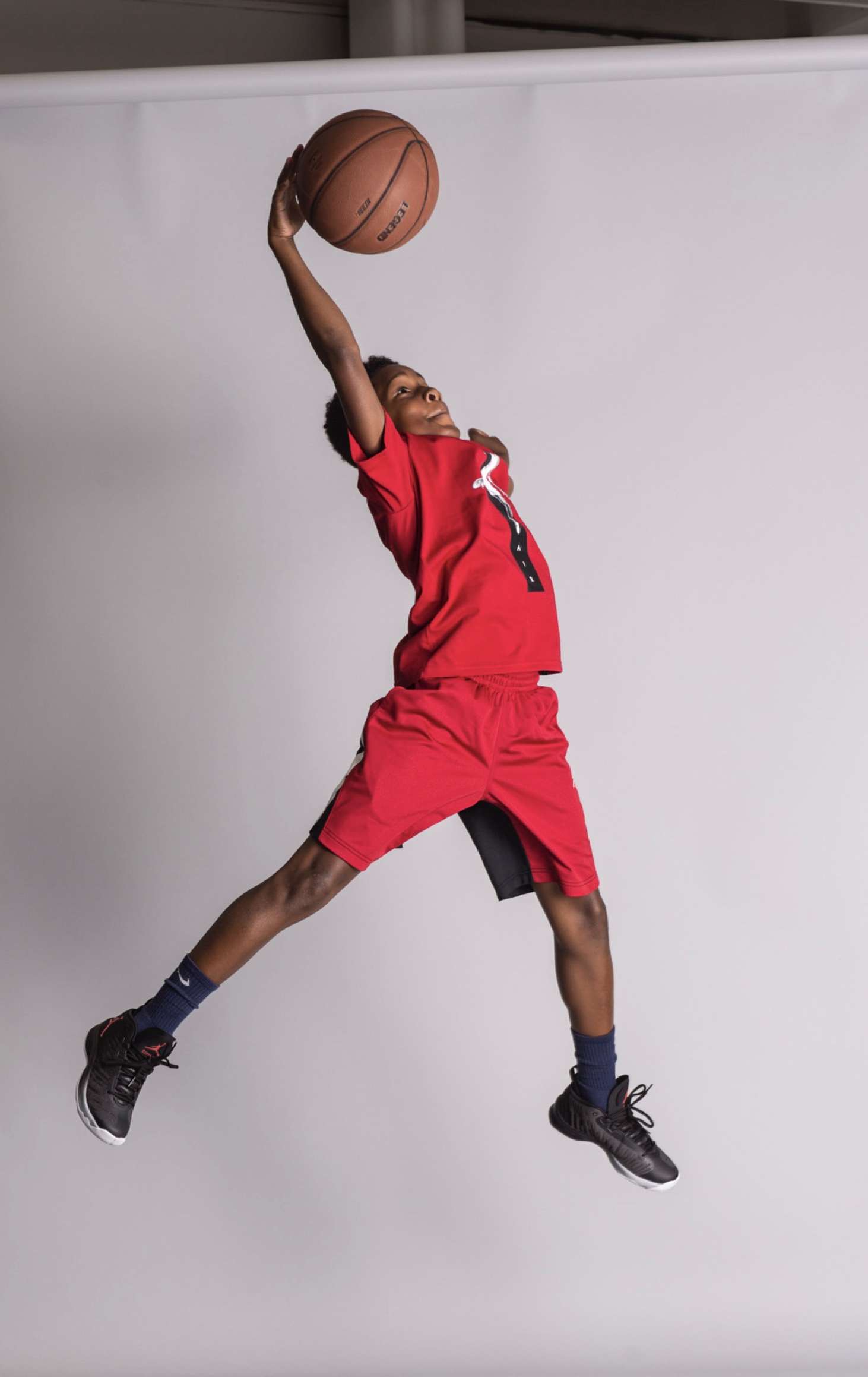 A boy is leaping in the air with a basketball, mimicking the Air Jordan logo.