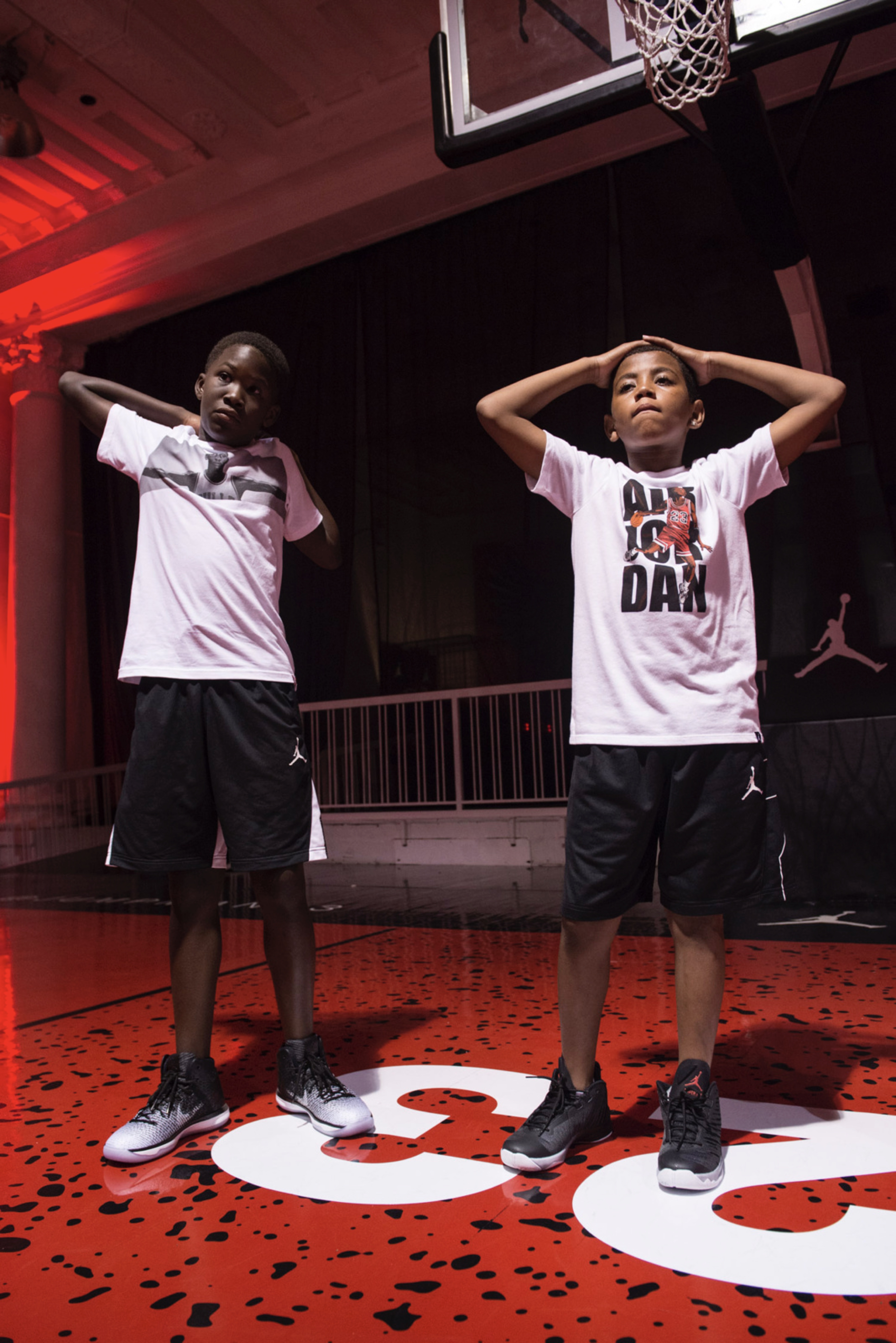 Two boys wearing Air Jordan clothing stand on a red indoor court.