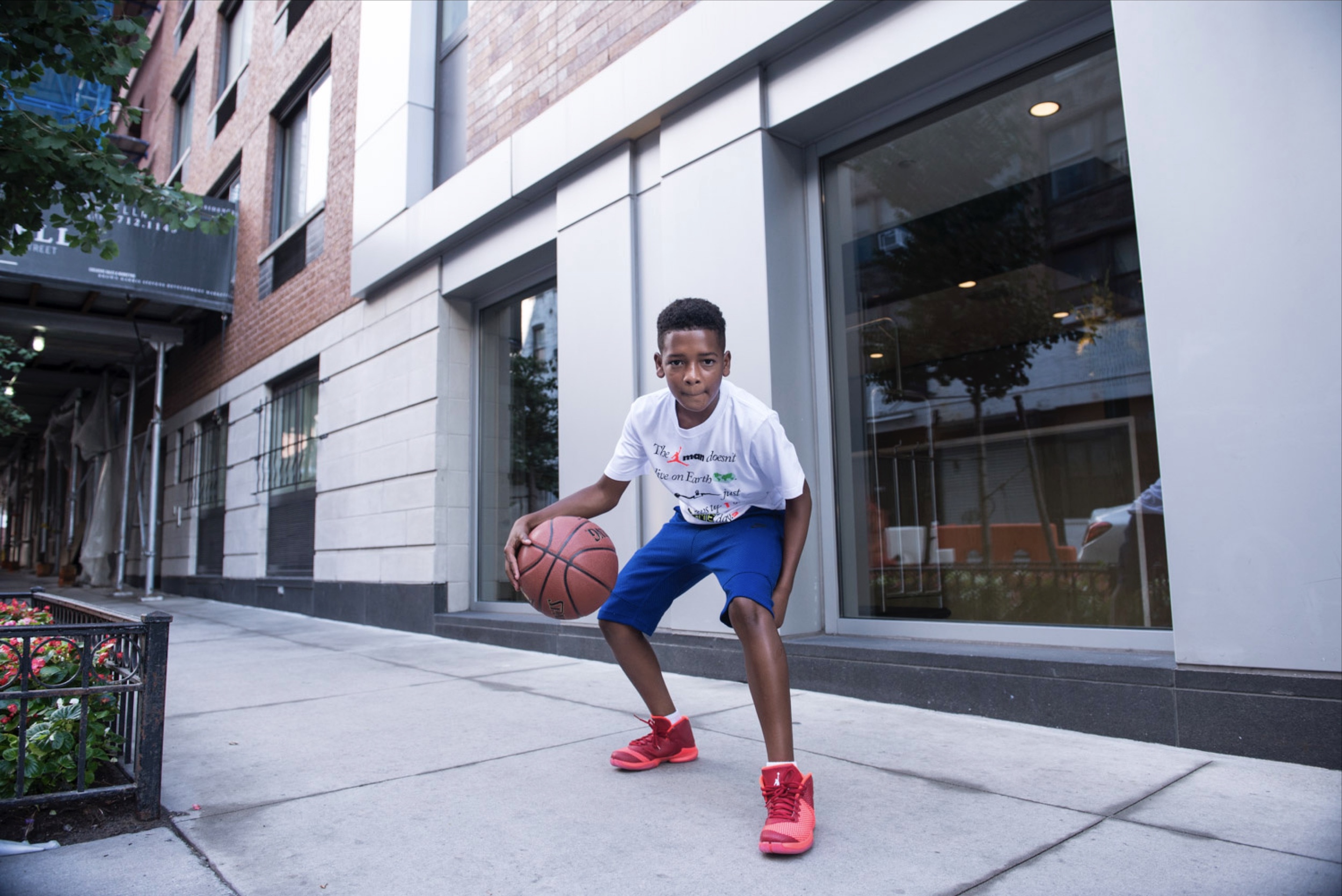 A boy dribbles a basketball outside on the sidewalks.