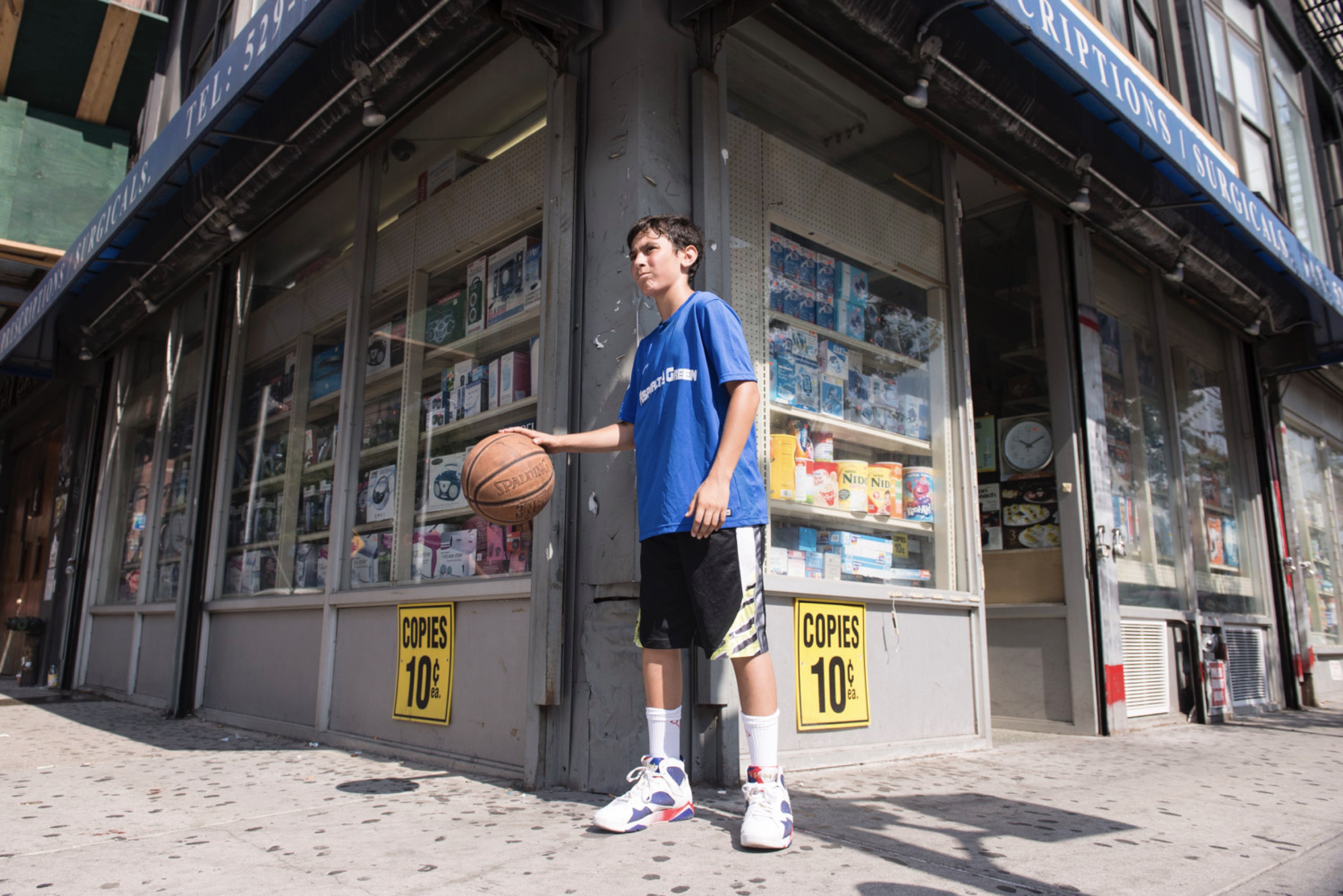 A boy dribbles a basketball on a street corner outside.