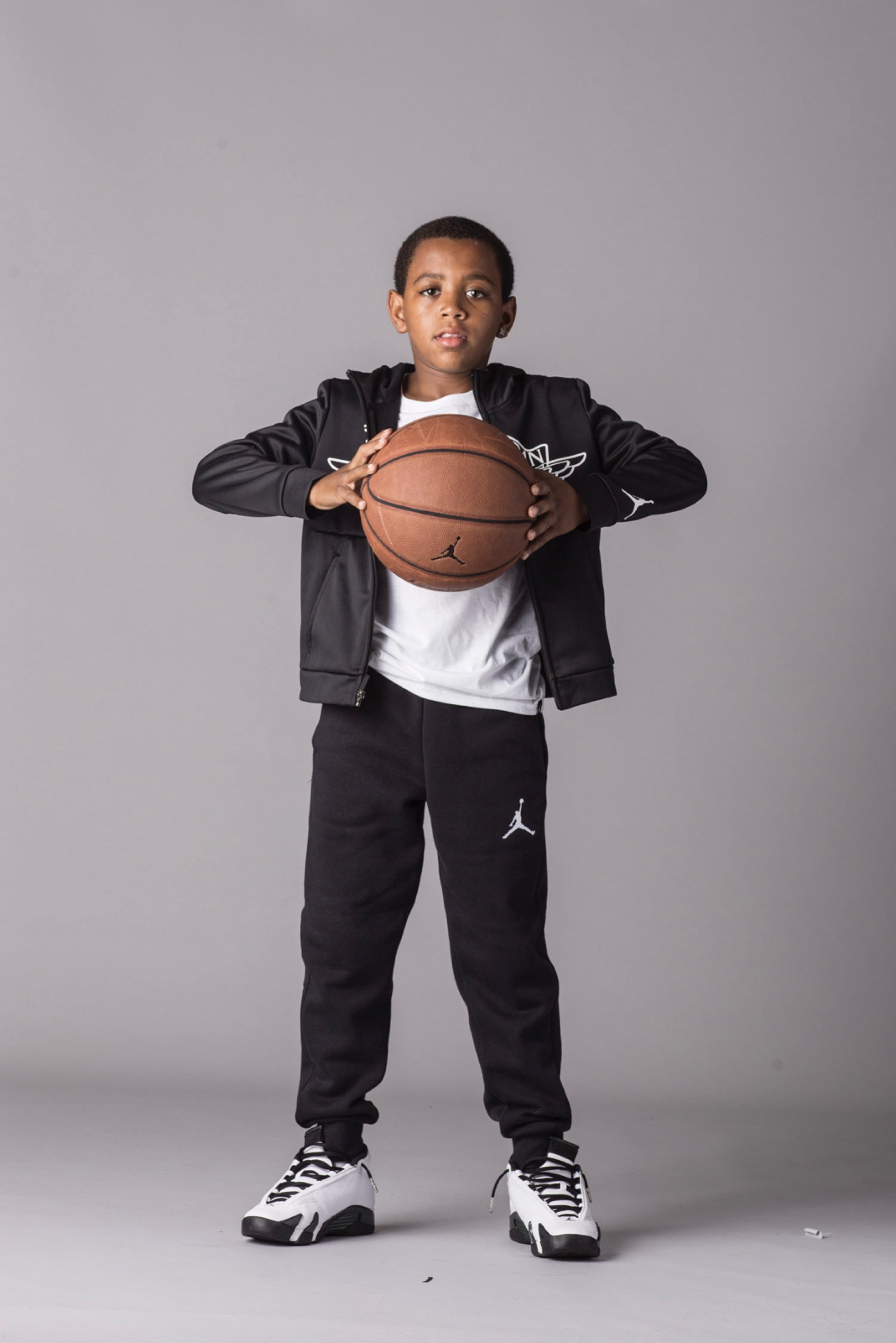 A boy wearing Jordan branded clothing holds a basketball in front of his chest.