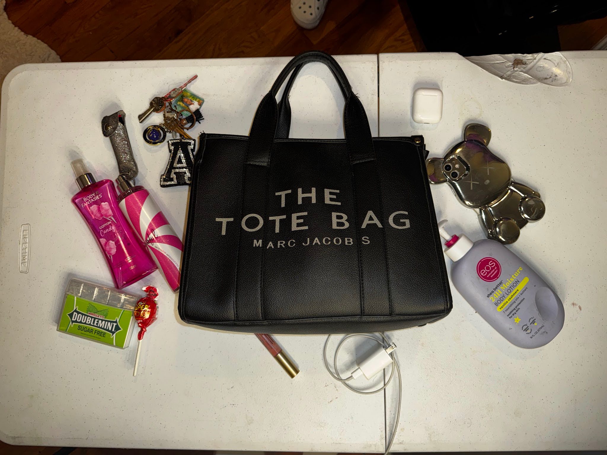 A tote bag with Marc Jacobs branding on a table surrounded by lotion, keys, a phone, and other objects commonly found in purses.