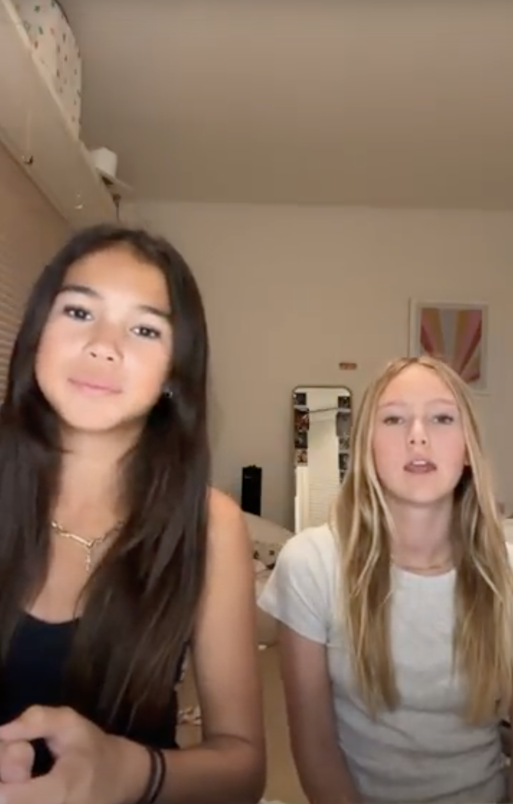 Two girls sitting in a room, talking to the camera.