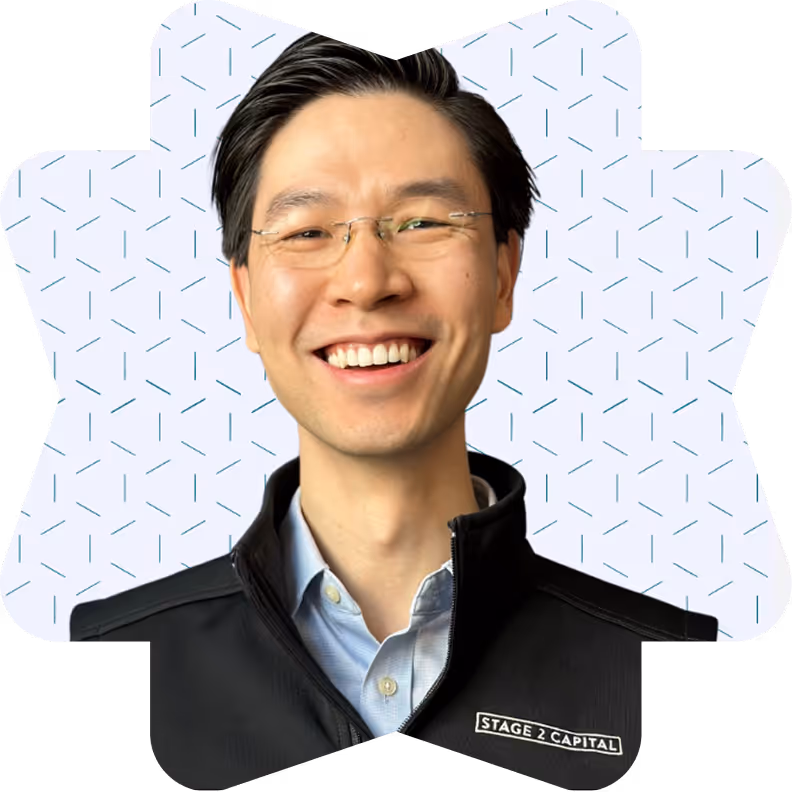 Smiling man wearing glasses, a light blue shirt, and a black jacket with Stage 2 Capital logo.