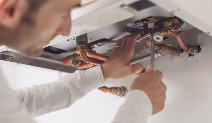 Handwerker repariert Kupferrohre unter einem Heizgerät mit einem Schraubenschlüssel.