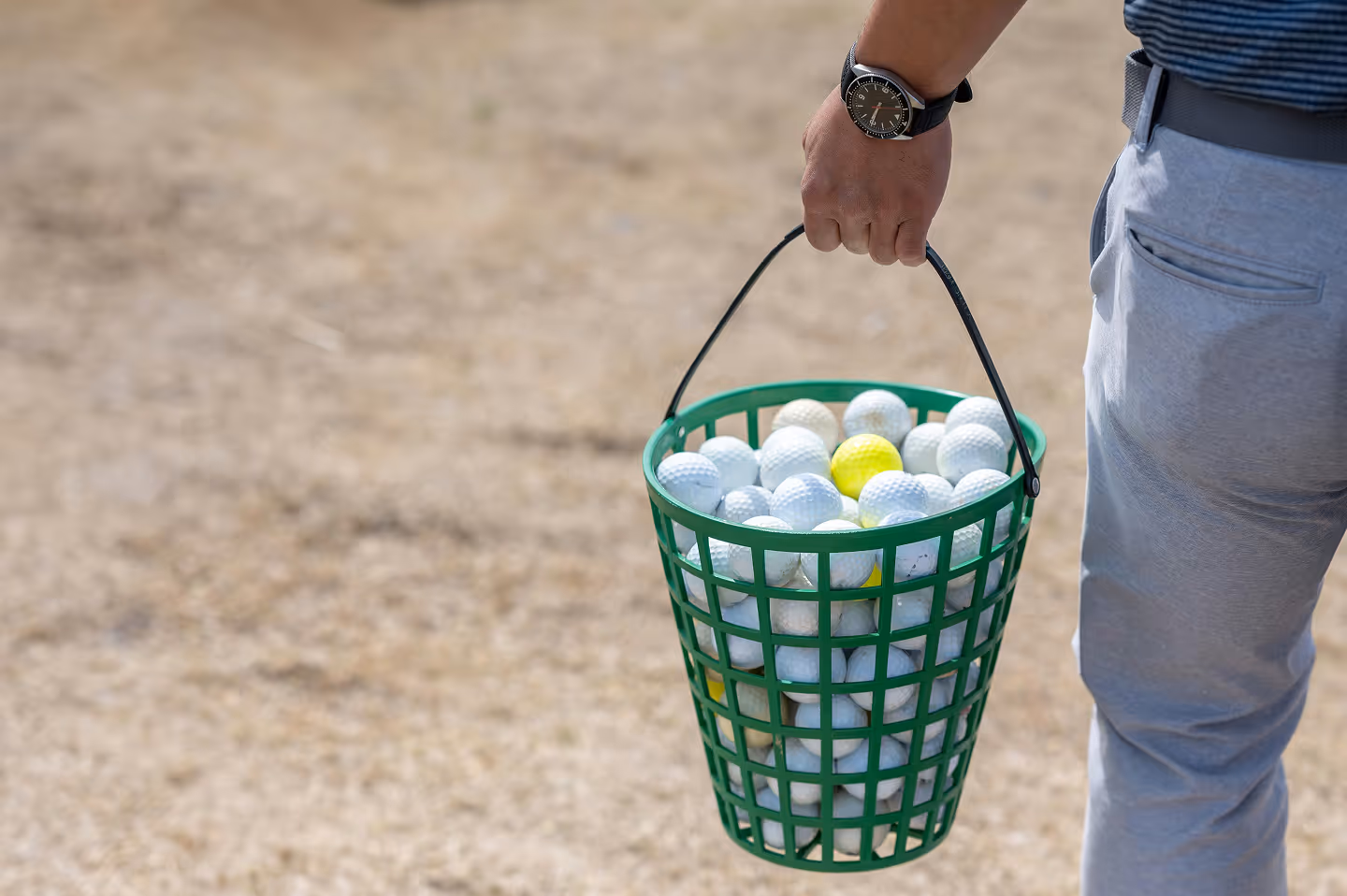Person holding a green basket filled with white and yellow golf balls.