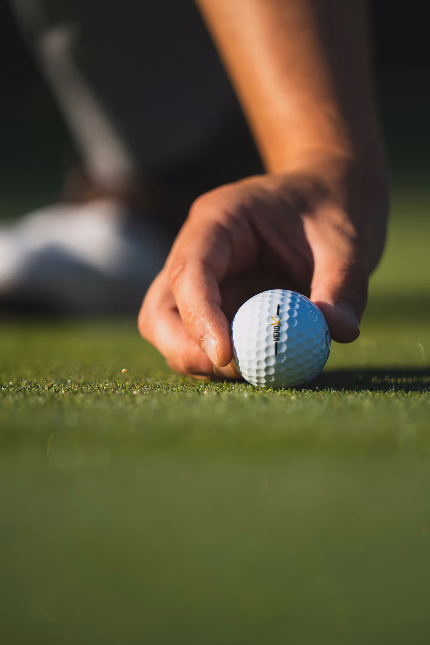 Hand placing a golf ball on green grass, focusing on the ball and fingers.