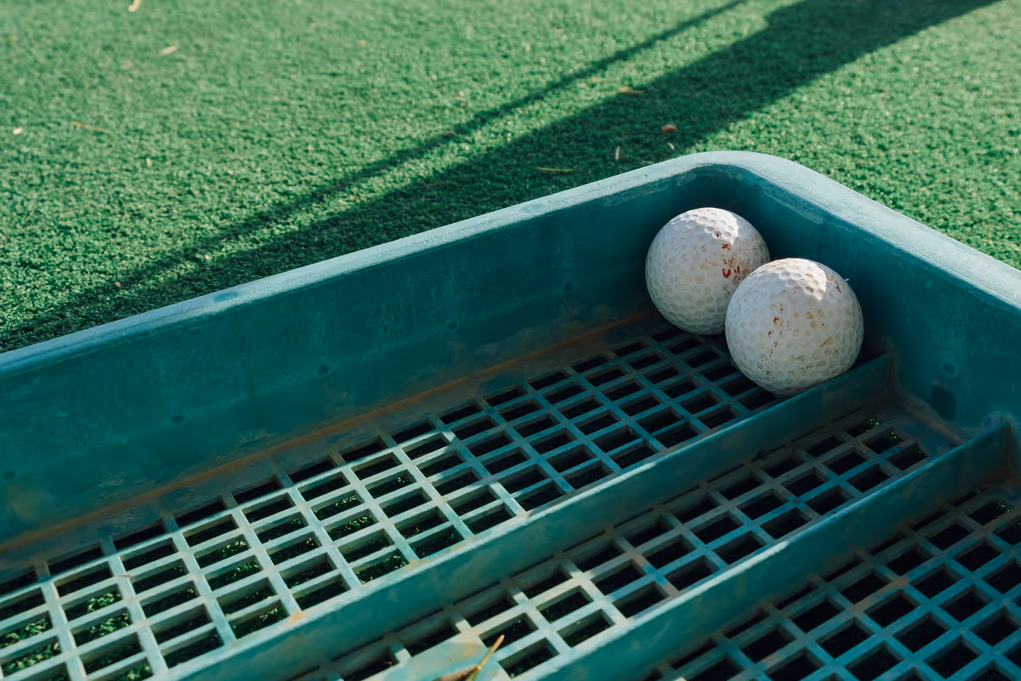 Two white golf balls resting in a green plastic golf ball tray on artificial turf.