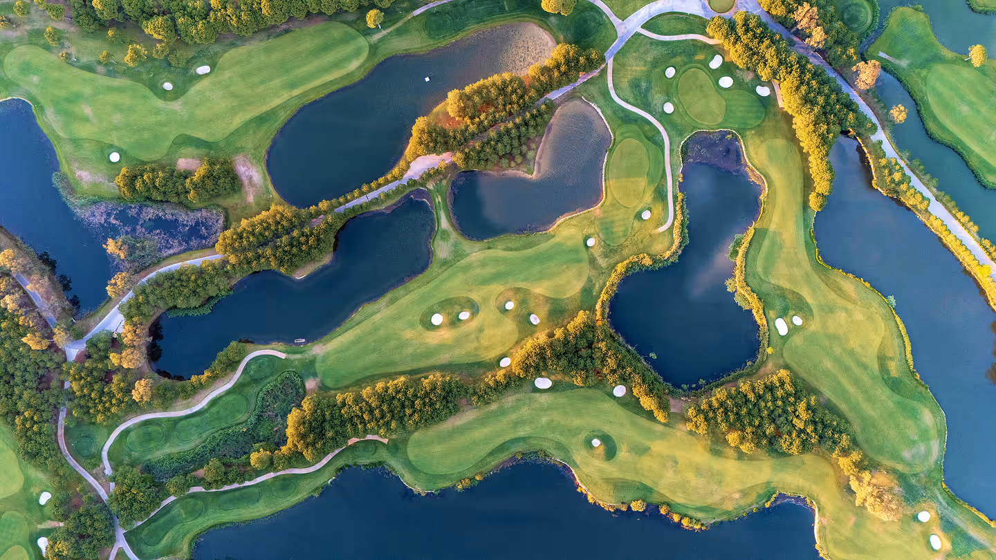 Aerial view of a golf course with several fairways, sand bunkers, water hazards, and surrounding trees.