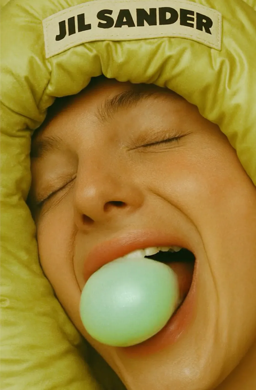 Close-up of model blowing bubblegum wearing olive green Jil Sander puffer hood — AI advertising photography by Nastassia Brame, Detroit AI Production House