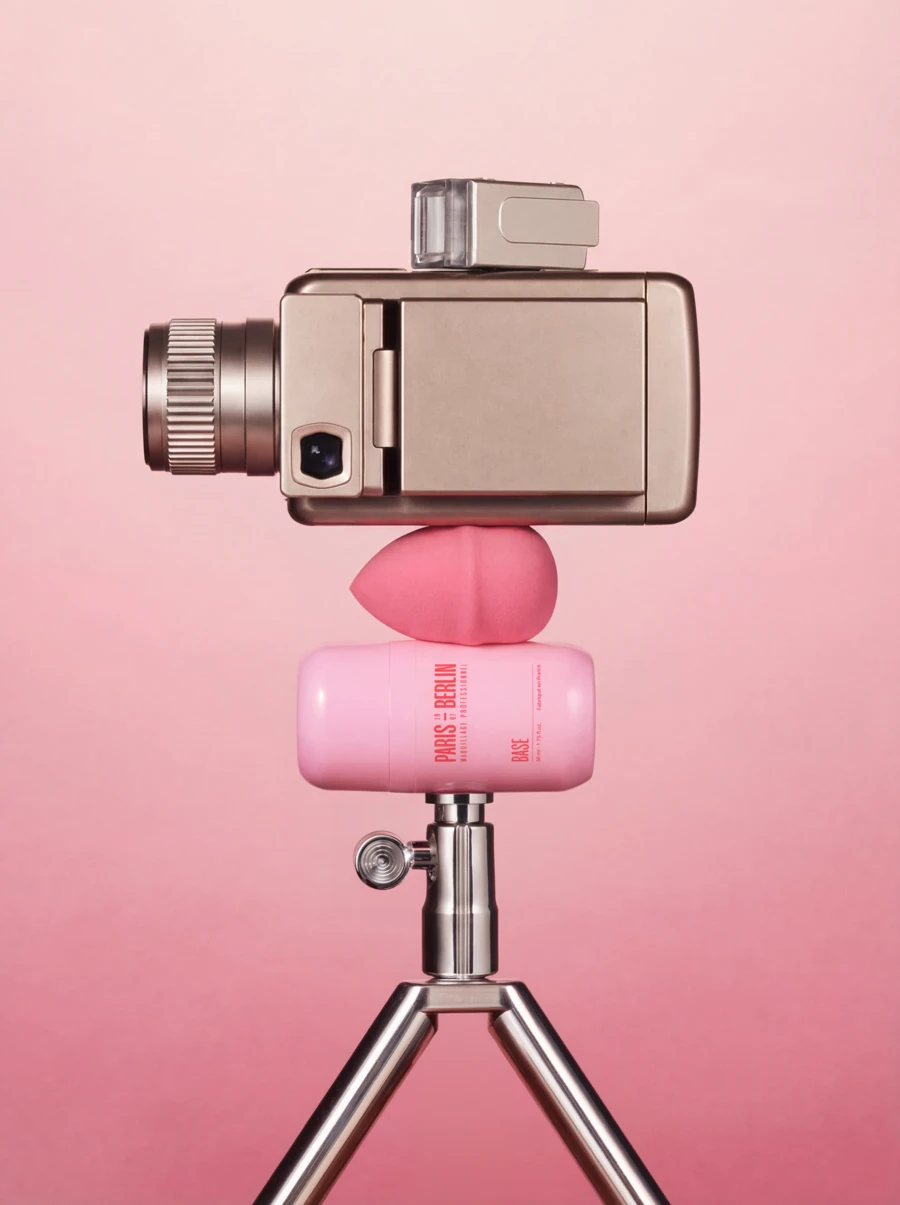 Paris Berlin foundation bottle and beauty sponge balanced beneath a vintage camera on a tripod, print campaign — 3d product visualization by Detroit AI Production House, photography & art direction by SQUAD