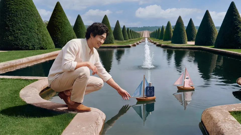 Man crouching by a garden pool, launching a toy sailboat carrying a Parfums de Marly bottle — ai film production Detroit, photography & DA by Alex