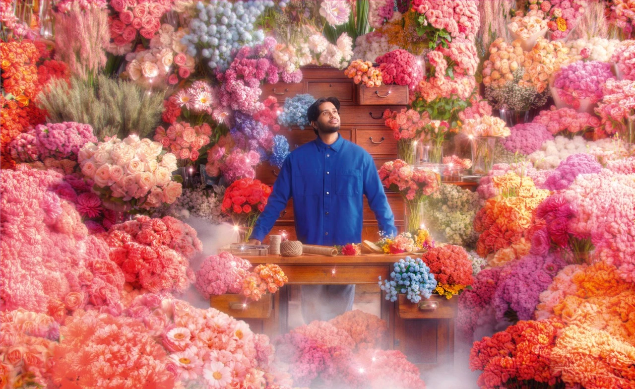 Man in blue shirt standing at a wooden desk engulfed by an overflowing sea of pink and coral blooms for SumUp — ai video production Detroit, photography & art direction by Pierrick Jégou