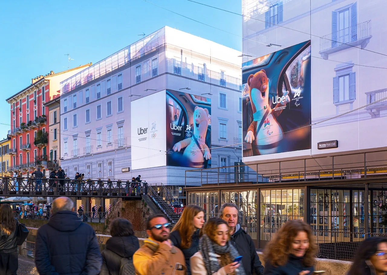 Giant Uber x Milano Cortina 2026 mascot wraps covering building facades above Milan's Navigli canal — ai advertising agency Detroit, photography & art direction by Detroit AI Production House