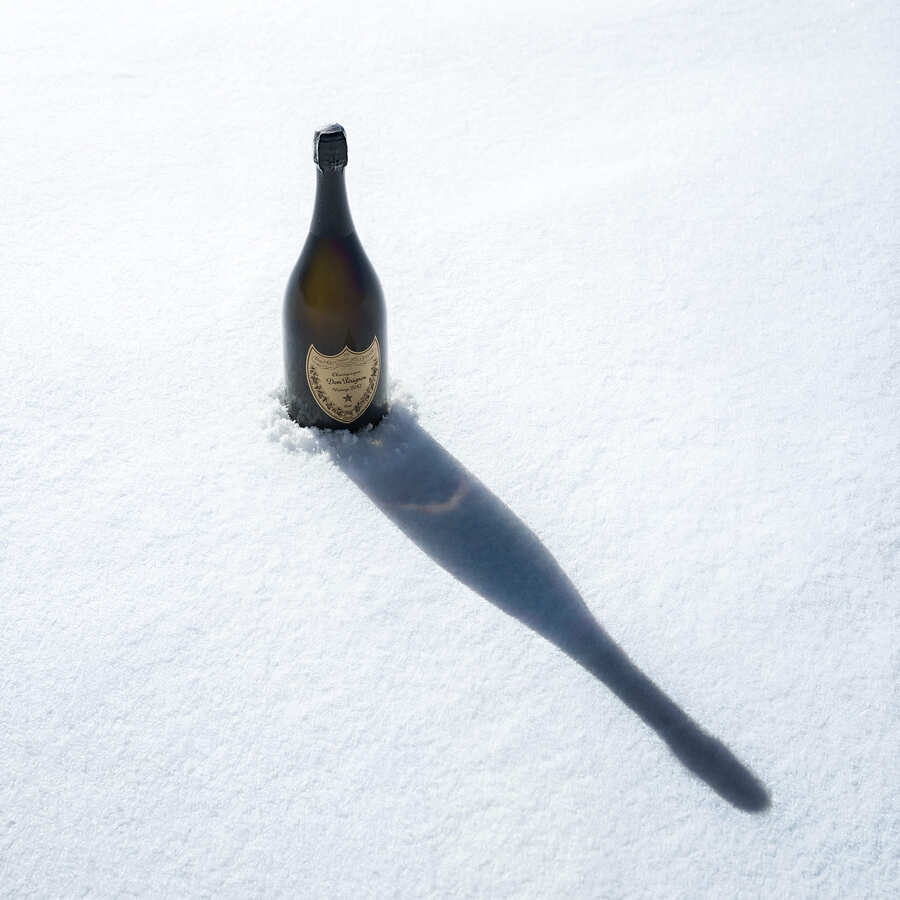Dom Pérignon bottle standing upright in fresh snow, casting a long diagonal shadow under bright sunlight — 3d product visualization Detroit, photography & art direction by Pierrick Jégou