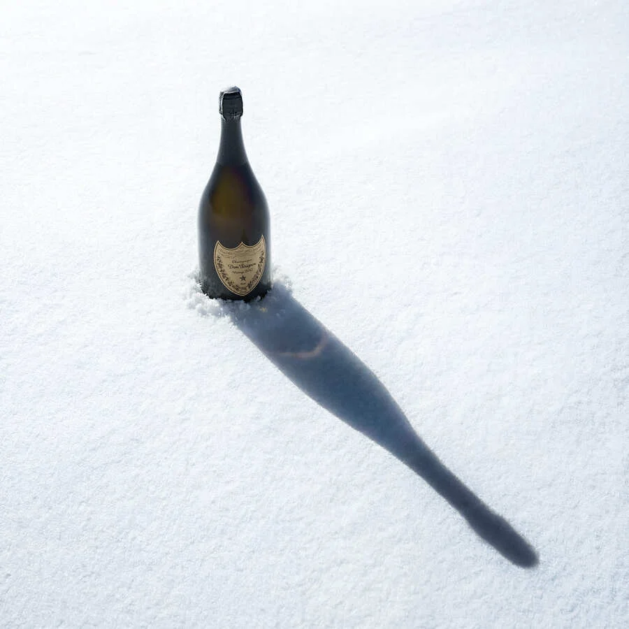 Dom Pérignon bottle standing upright in fresh snow, casting a long diagonal shadow under bright sunlight — 3d product visualization Detroit, photography & art direction by Pierrick Jégou