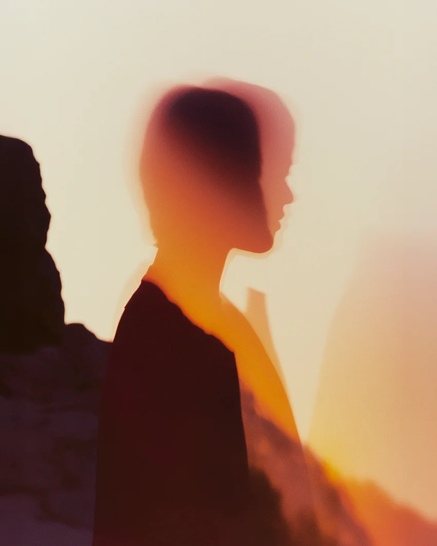 Soft-focus profile silhouette of a woman bathed in warm golden light beside dark rock formations — ai advertising agency Detroit, photography & art direction by Pierrick Jégou, produced by Detroit AI Production House